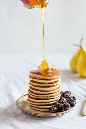 Stack of pancakes on white with honey drizzled on top