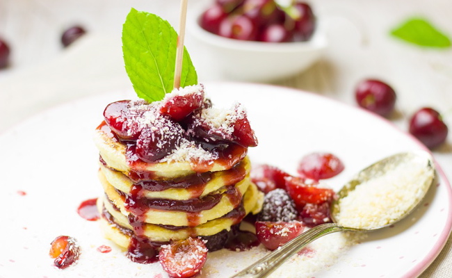 Plate of pancakes, stacked with red syrup and cherries on top