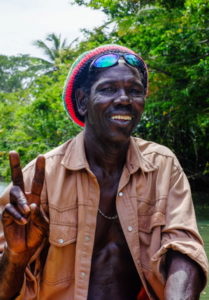Dark-skinned man in Rasta hat and sunglasses, making peace sign with fingers