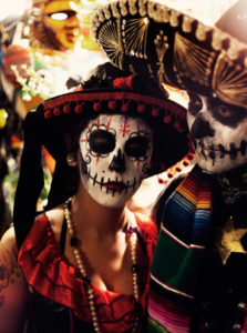 Woman looking at camera with face paint, man at side, Dia de los Muertos skeleton