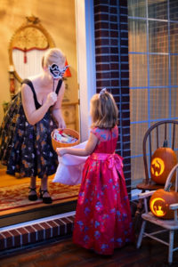 Girl in dress at door of woman in mask, pumpkins, Halloween