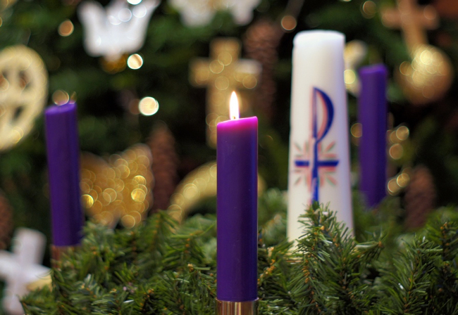 Purple candle lit, sitting in evergreen wreath with other candles