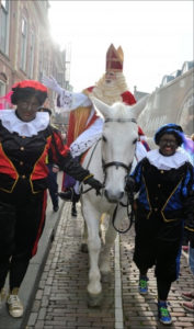 White horse carrying man in red robes with white beard, two people guide horse in front