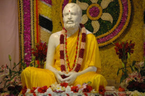White statue of man sitting, decorated with yellow robe and flowers