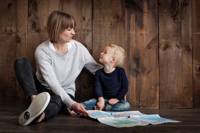 Woman and young boy sitting on wood floor, looking at each other, map on floor